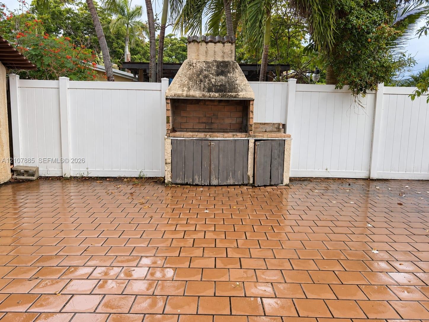 Outdoor patio featuring a paved tile floor, built-in masonry grill, and white vinyl privacy fencing