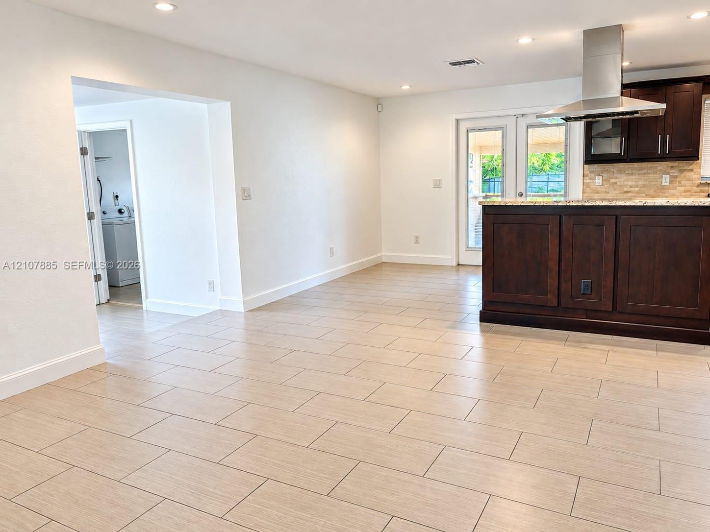 Kitchen featuring dark wood cabinetry, stone-finish countertops, stainless steel chimney-style range hood, and tile flooring