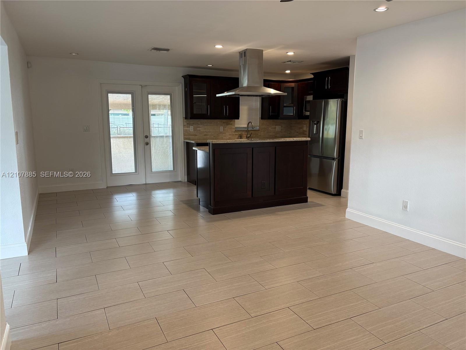 Kitchen featuring dark wood-finish cabinetry, stone countertops, stainless steel appliances, a stainless steel range hood, and tile flooring