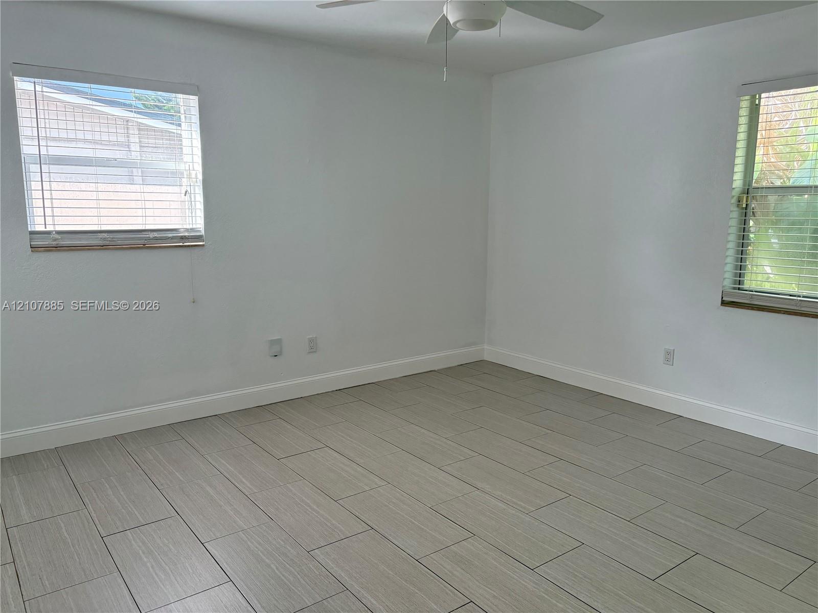 Interior room featuring neutral wall finishes, tile flooring, dual windows with horizontal blinds, and a ceiling fan