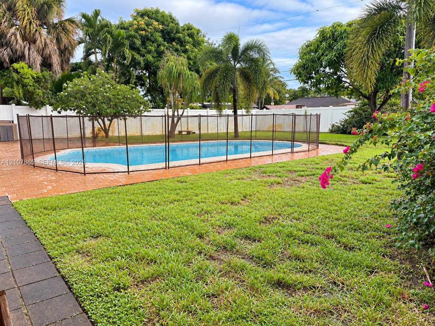 Backyard featuring an in-ground swimming pool, mesh safety fencing, paved patio, expansive lawn, and white perimeter privacy fencing