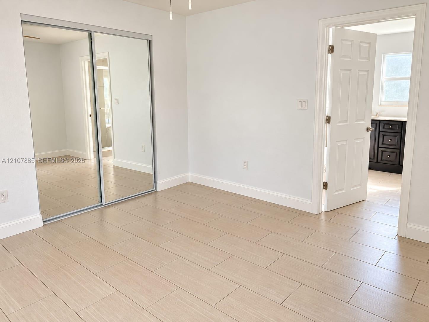 Room interior featuring light-toned tile flooring, mirrored sliding closet doors, and a six-panel interior door