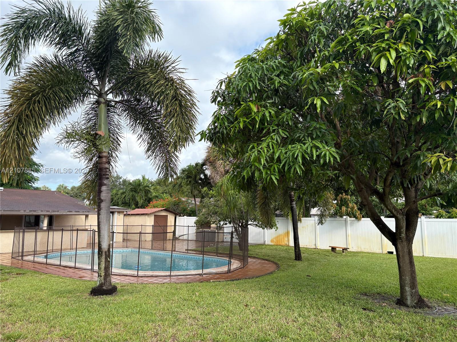 Backyard featuring a swimming pool, safety fencing, mature landscaping, and a solid perimeter privacy fence