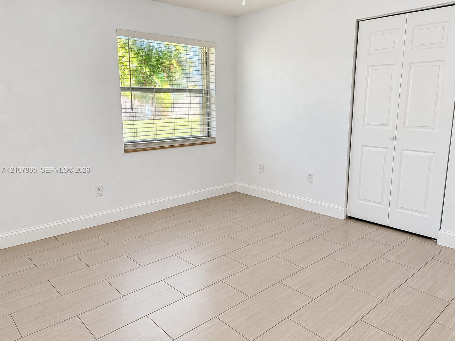 Neutral-toned wood-finish tile flooring, white bi-fold closet doors, and horizontal window blinds