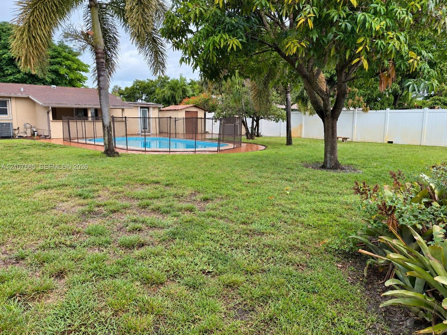 Backyard featuring an in-ground swimming pool, perimeter safety fencing, mature trees, and a solid-panel privacy fence