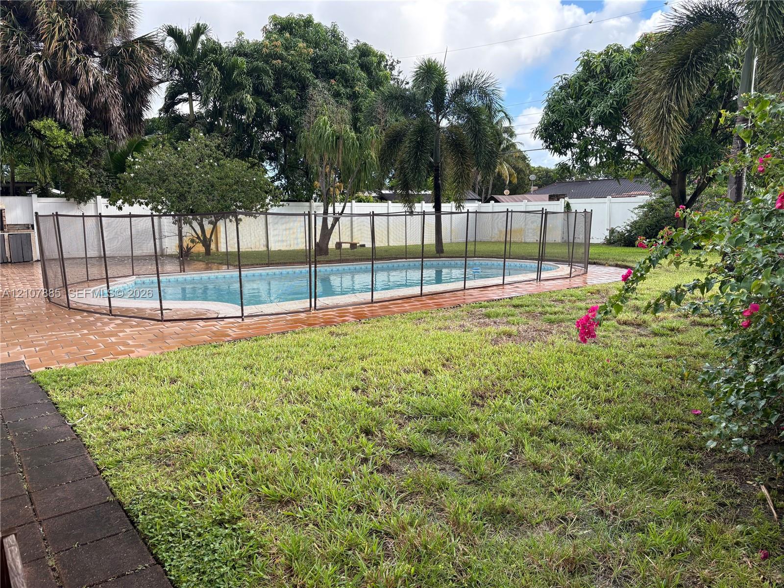 Backyard featuring an in-ground swimming pool, mesh safety fencing, paver patio, lawn, and perimeter privacy fencing