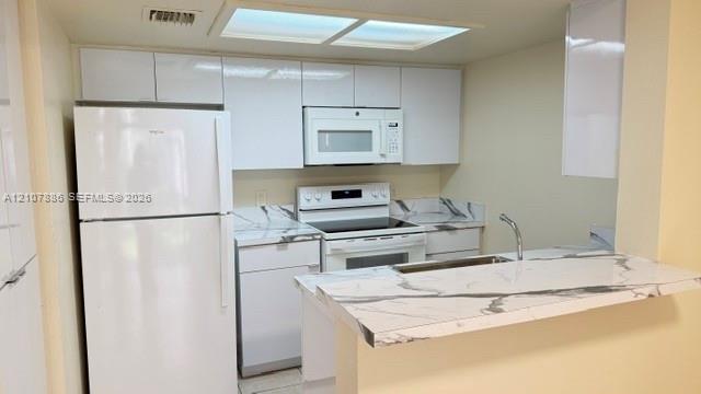 Kitchen featuring high-gloss white cabinetry, stone-patterned countertops, a stainless steel sink with a goose-neck faucet, and white appliances including a built-in microwave and range