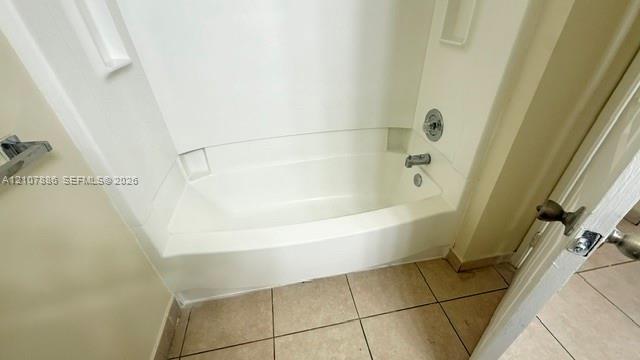 Bathtub and shower combination featuring a white molded surround with integrated storage niches, chrome-finish faucet hardware, and ceramic tile flooring