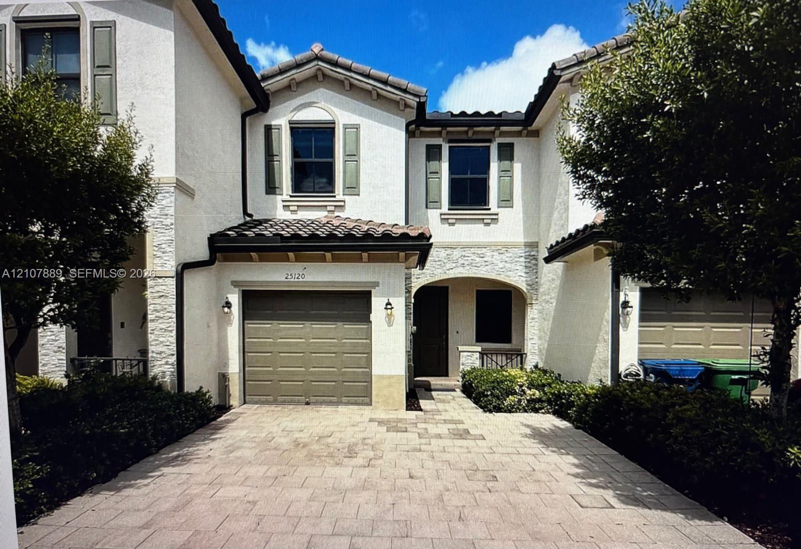 Stucco exterior featuring stacked stone accents, paver driveway, arched entryway, and tile roof