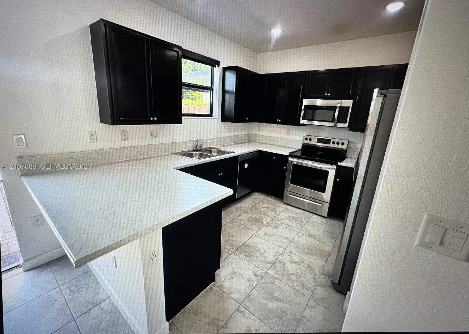 Kitchen featuring dark cabinetry, stone-finish countertops, stainless steel appliances, a dual-basin sink, and tile flooring