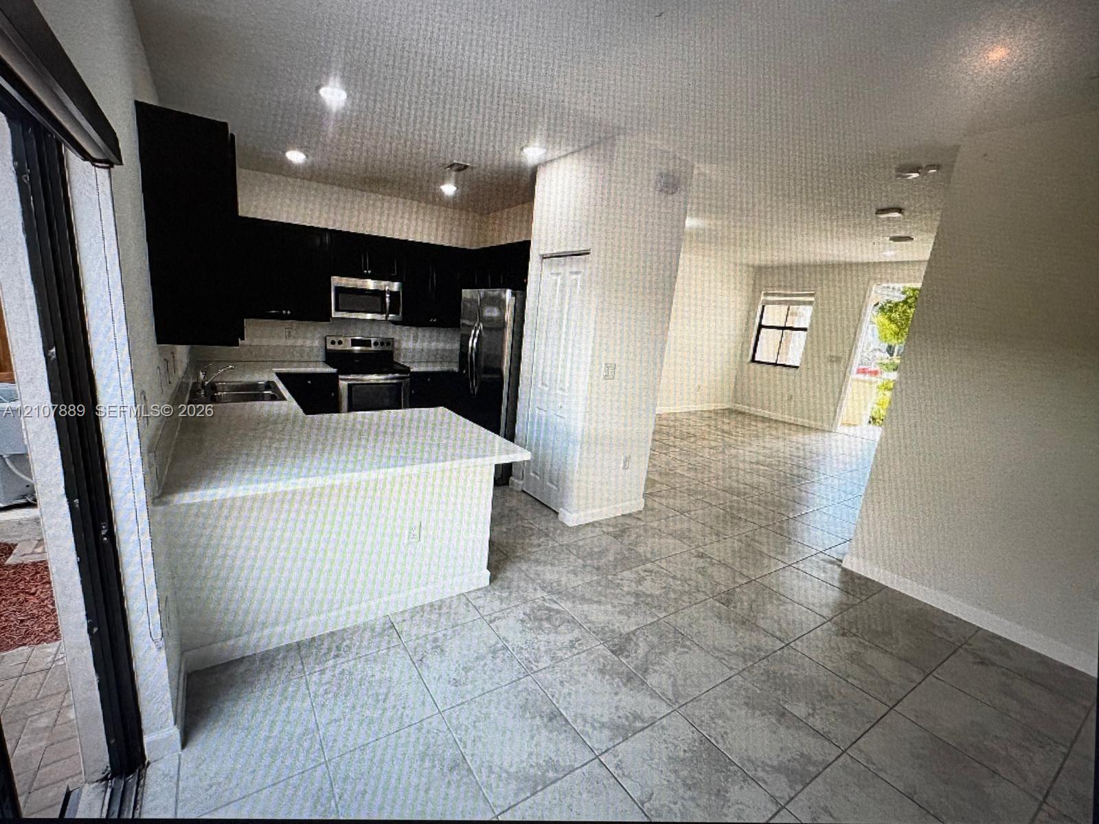 Kitchen featuring dark cabinetry, stone-finish countertops, stainless steel appliances, and tile flooring