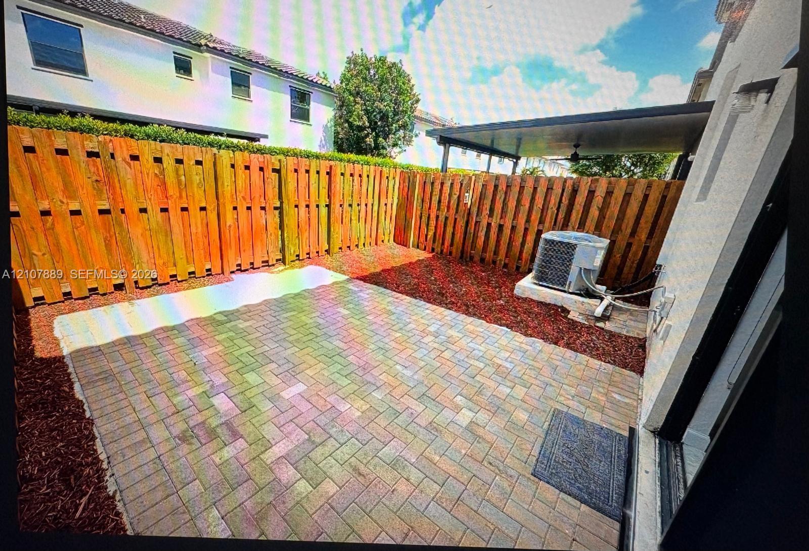 Rear patio featuring herringbone-patterned pavers, wood-slat privacy fencing, and a covered pergola