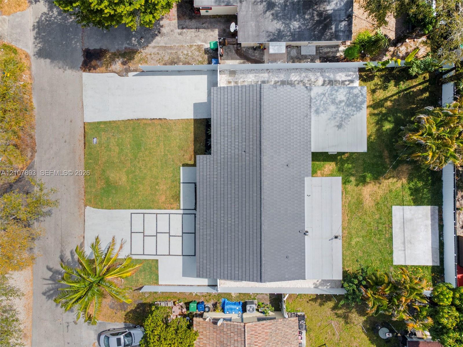 Aerial view of a residential property featuring a gray shingle roof, a concrete driveway, a segmented paver patio area, and an expansive grass lawn