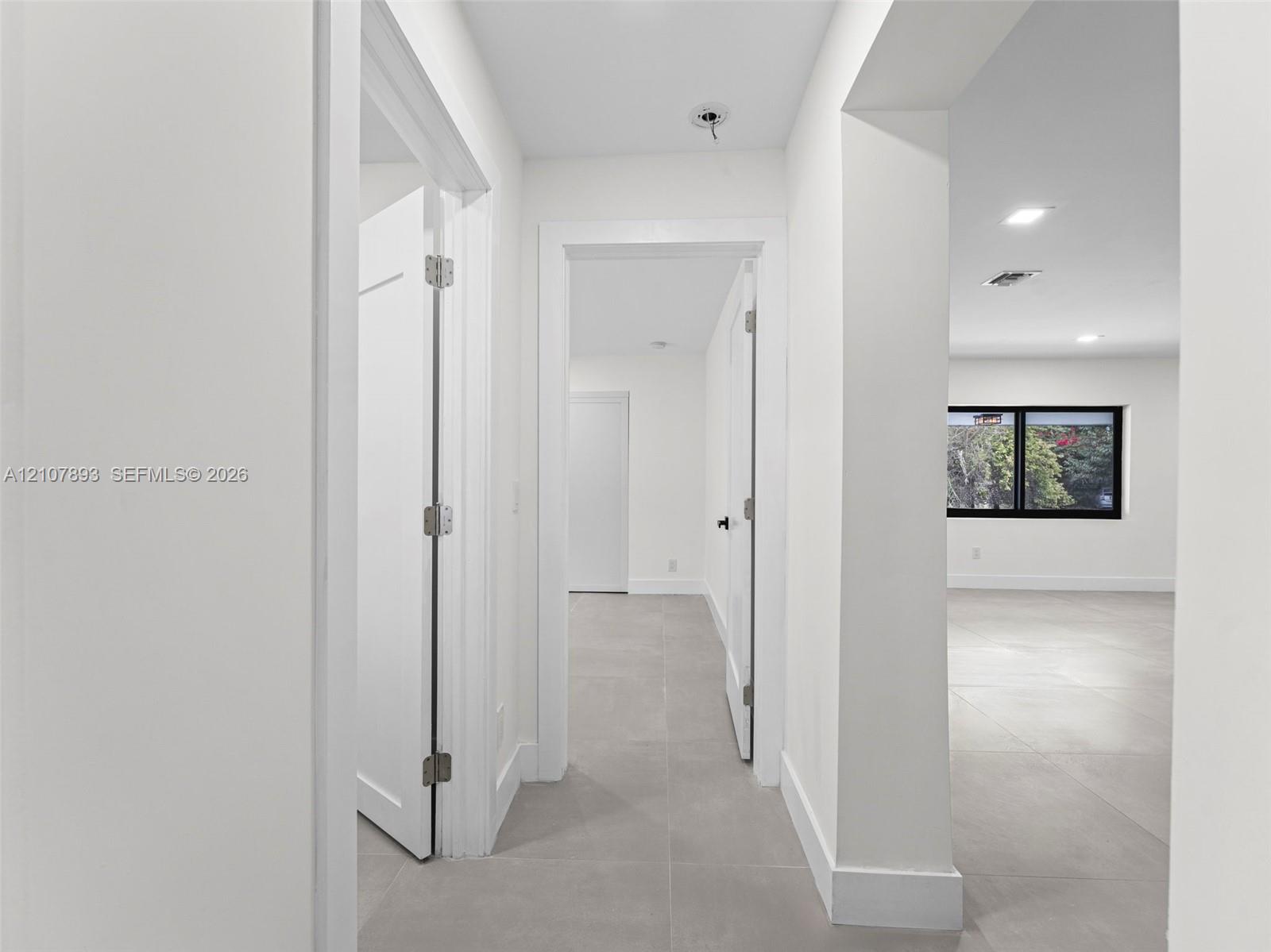 Neutral-toned large-format tile flooring, crisp white walls, recessed ceiling lighting, and black-trimmed window frames