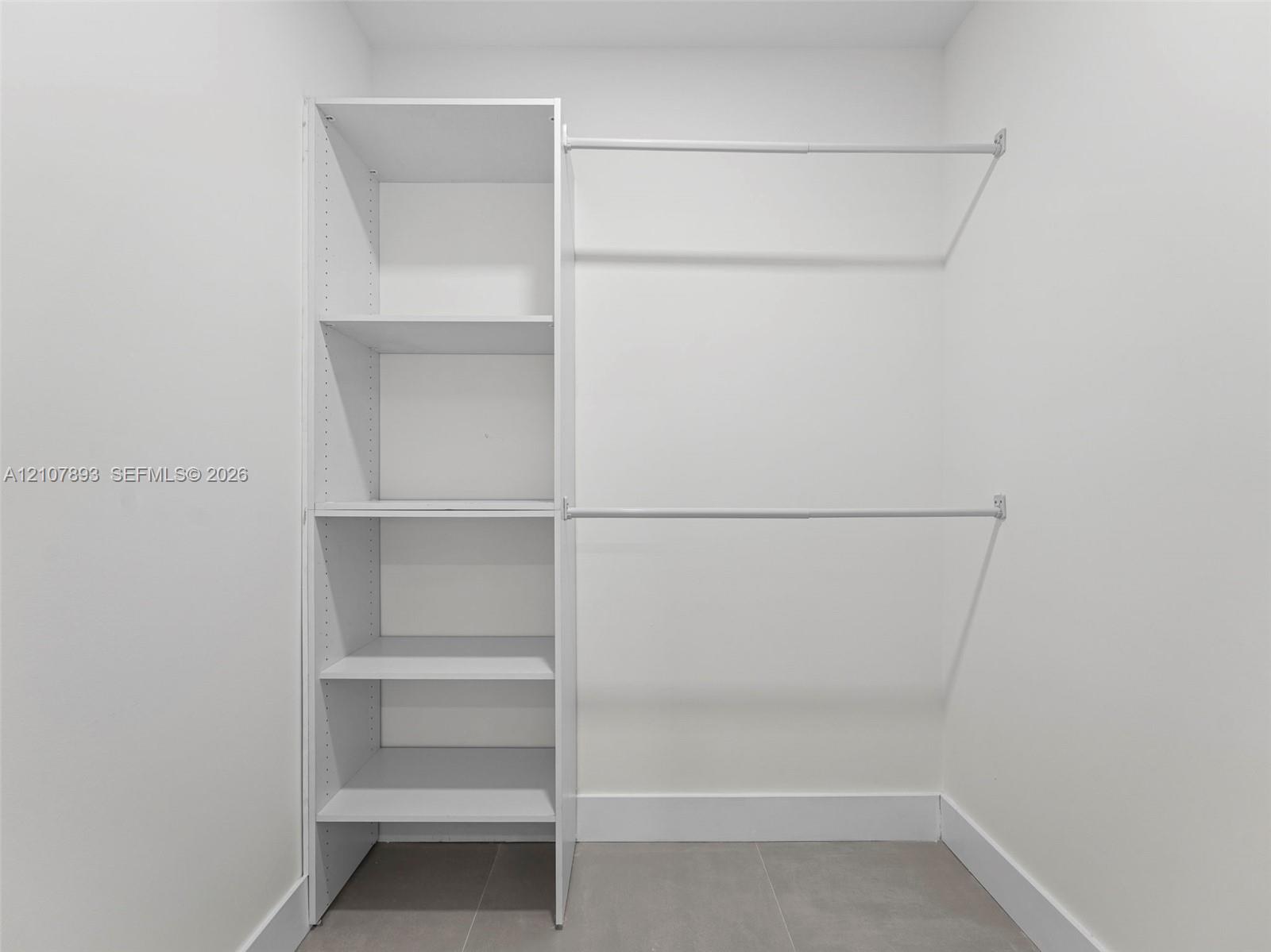 Walk-in closet featuring white built-in shelving and dual horizontal hanging rods over tile flooring