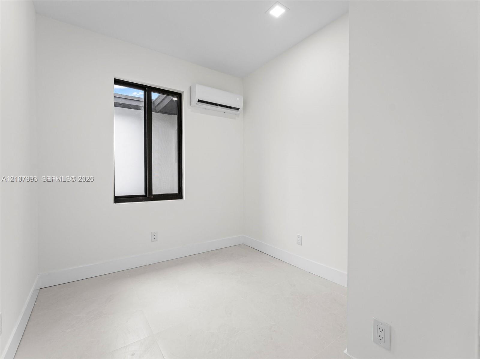 Neutral room featuring light-toned tile flooring, recessed ceiling lighting, a wall-mounted ductless air conditioning unit, and a window with a dark frame
