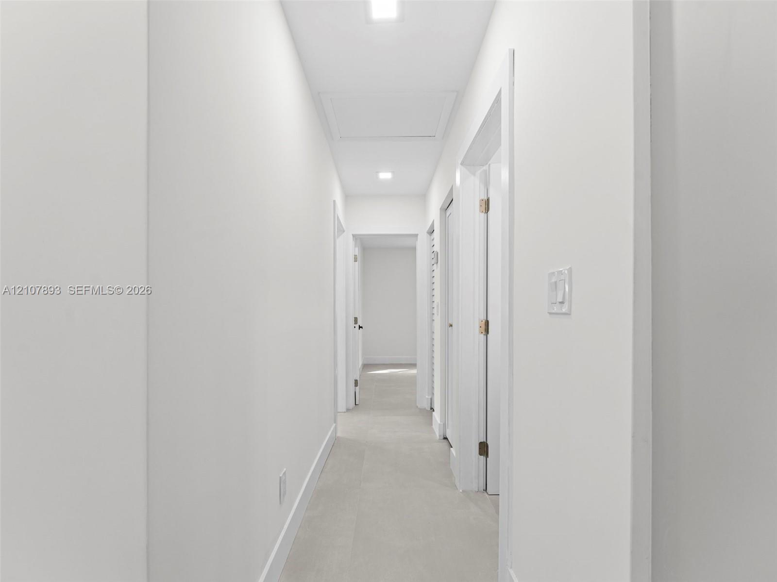 Hallway featuring neutral-toned tile flooring, recessed ceiling lighting, and crisp white wall finishes