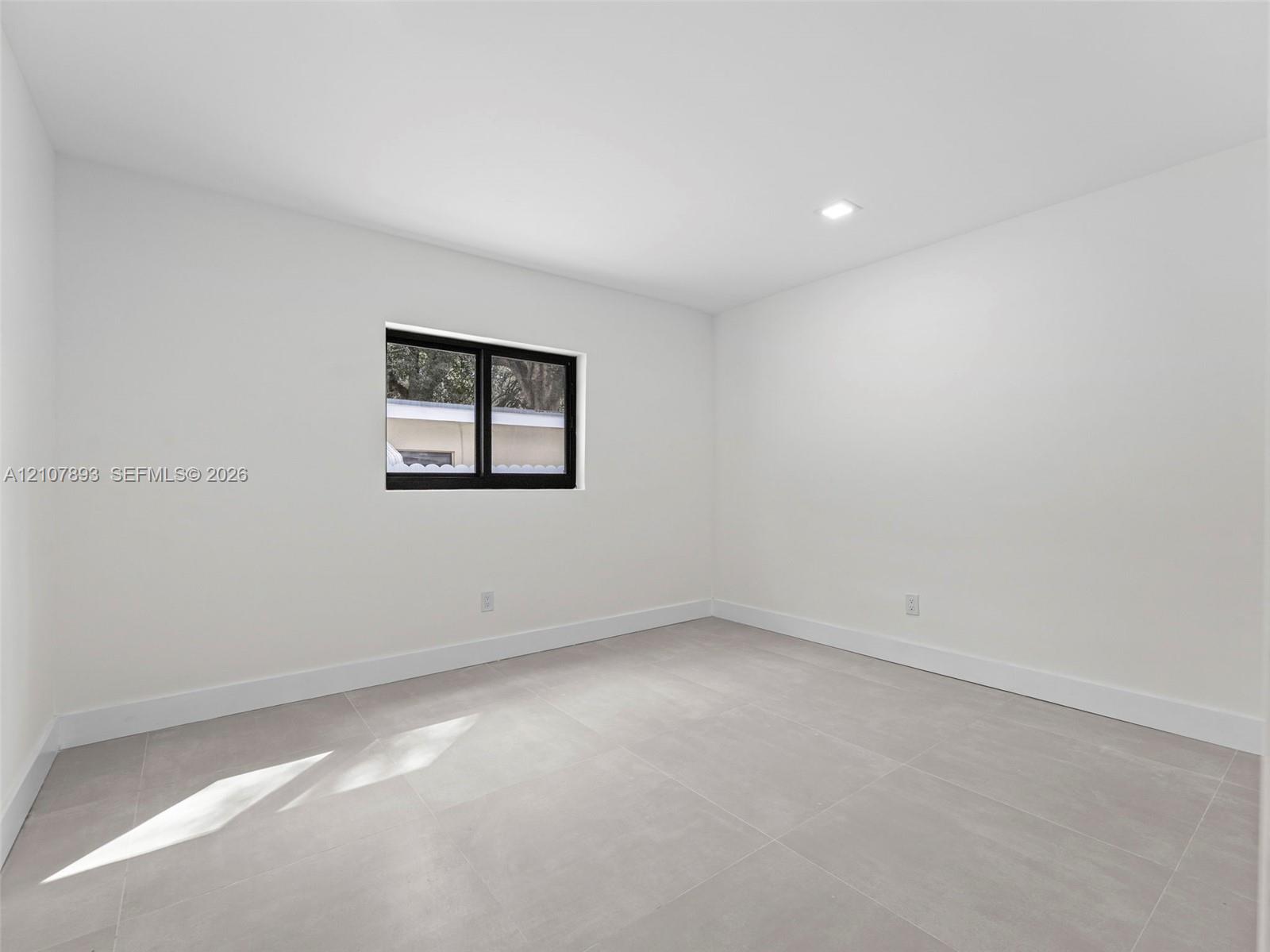 Neutral-toned tile flooring, recessed ceiling lighting, and a single-pane window with a black frame