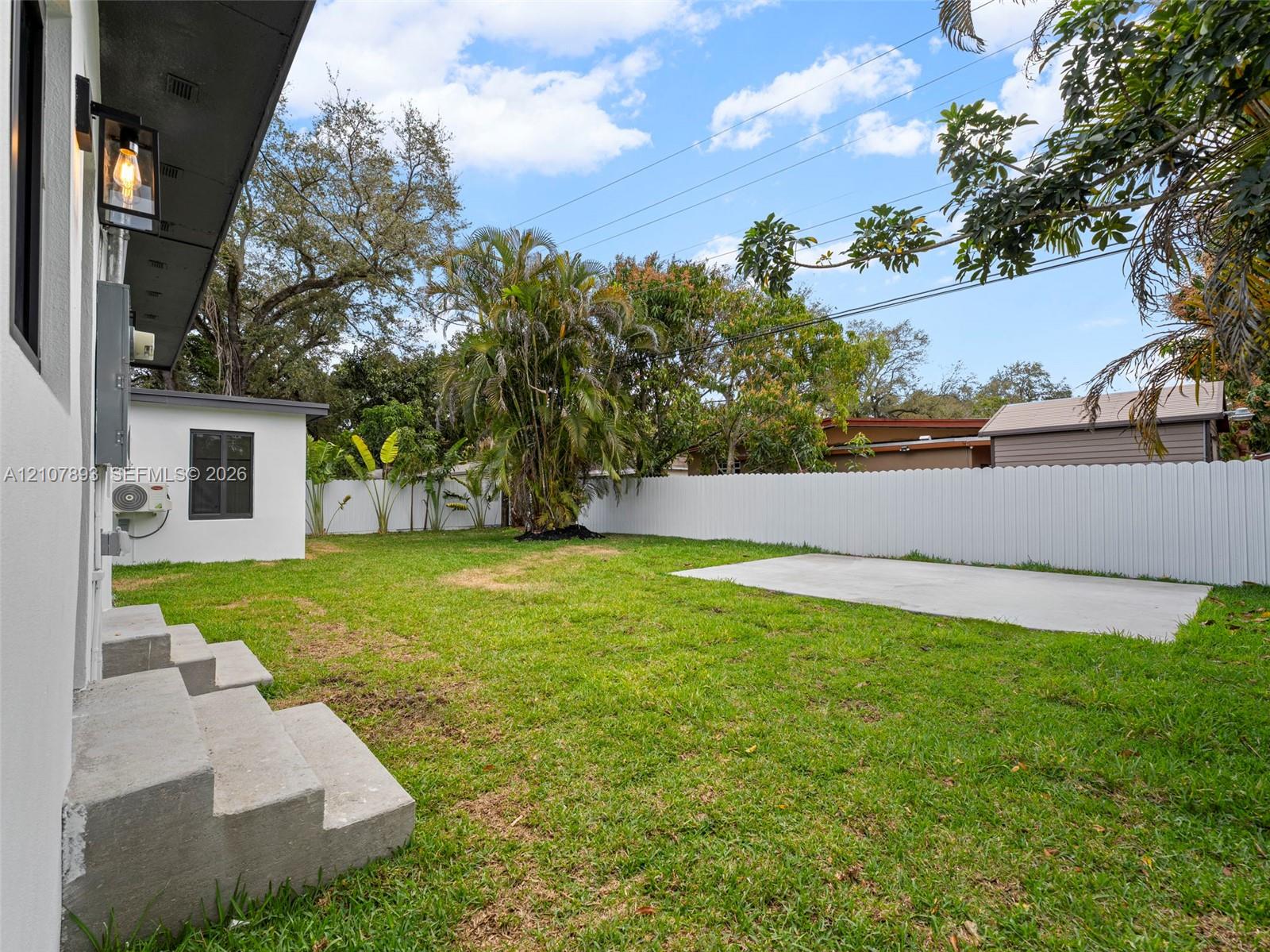 Fenced backyard featuring a manicured lawn, concrete patio, concrete stairs, and mature landscaping