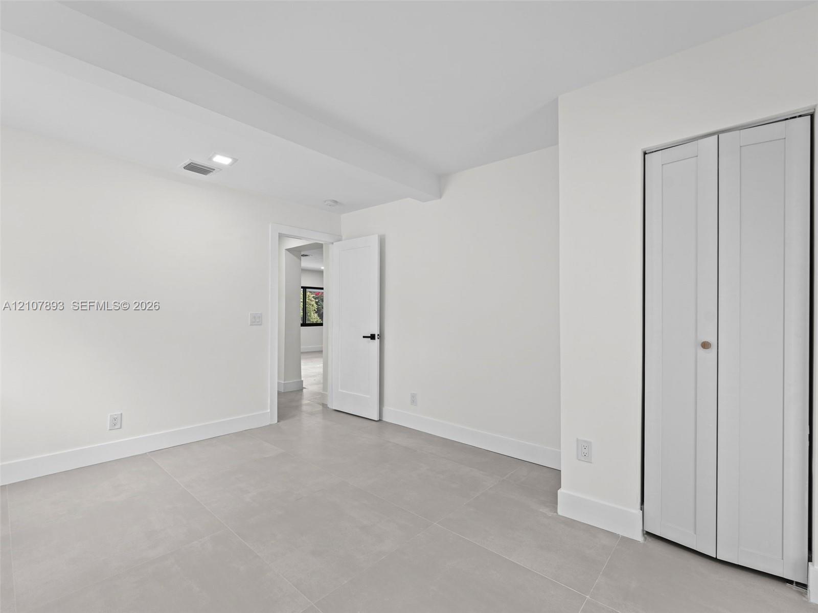 Neutral-toned interior featuring large-format tile flooring, crisp white wall finishes, a solid-core interior door with matte black hardware, and a classic-style bi-fold closet