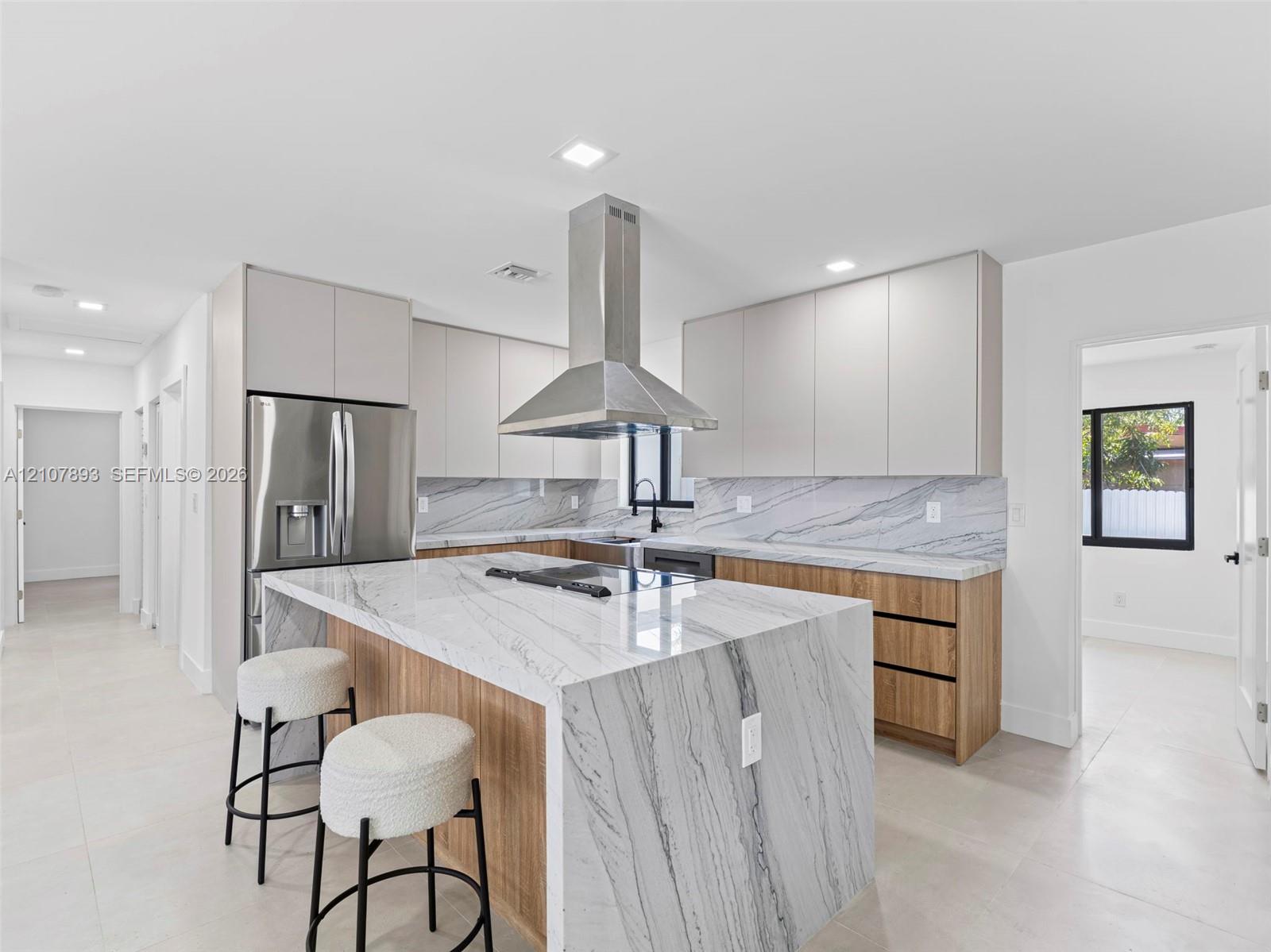 Kitchen featuring a waterfall-edge island with stone-finish countertop, dual-tone cabinetry, stainless steel range hood, and integrated cooktop