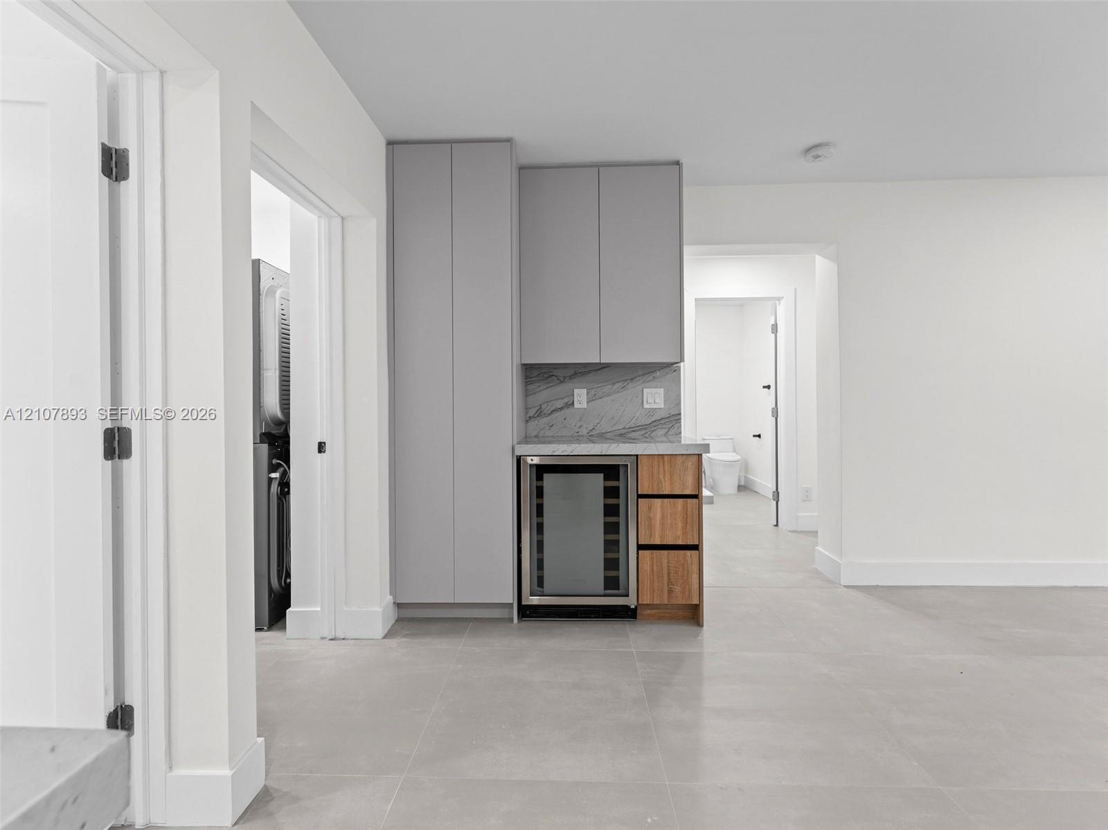 Built-in cabinetry featuring grey slab-front doors, integrated wine refrigerator, wood-finish drawers, and stone-finish backsplash