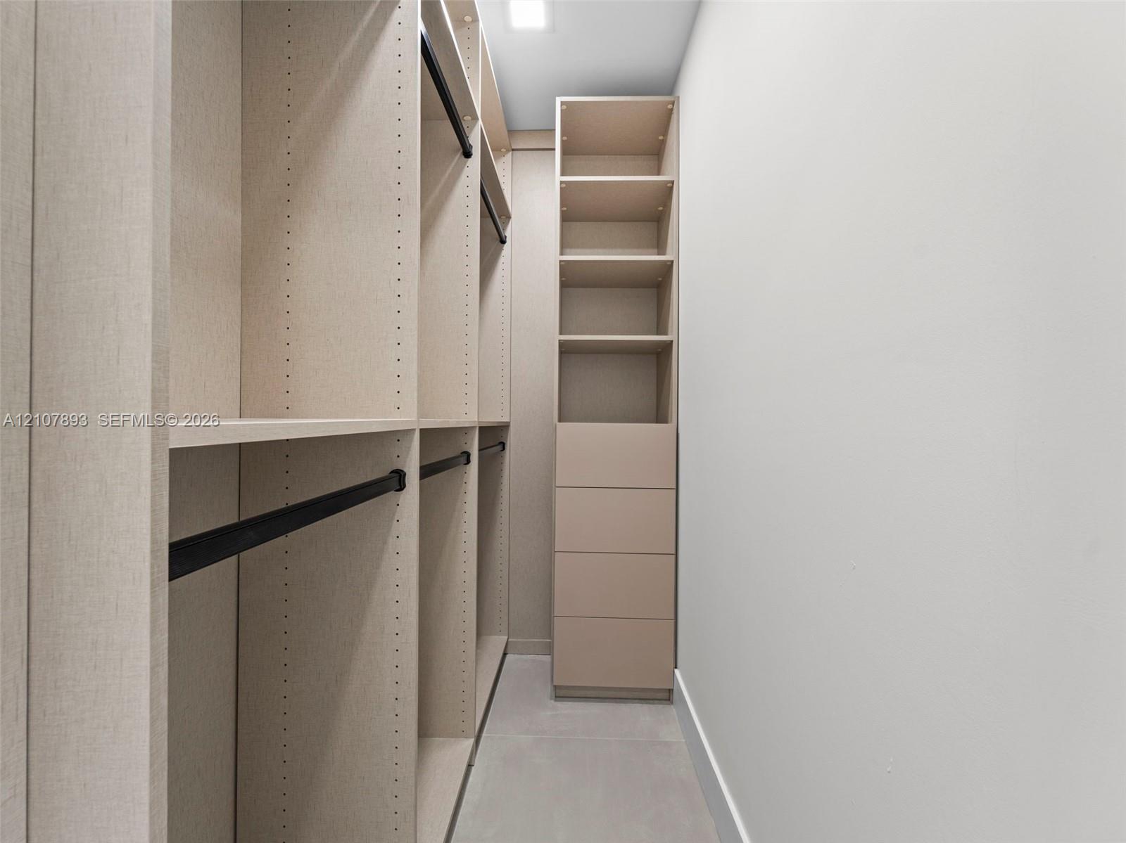 Custom built-in storage system featuring floor-to-ceiling shelving, integrated drawers, matte black hanging rods, and neutral-toned cabinetry