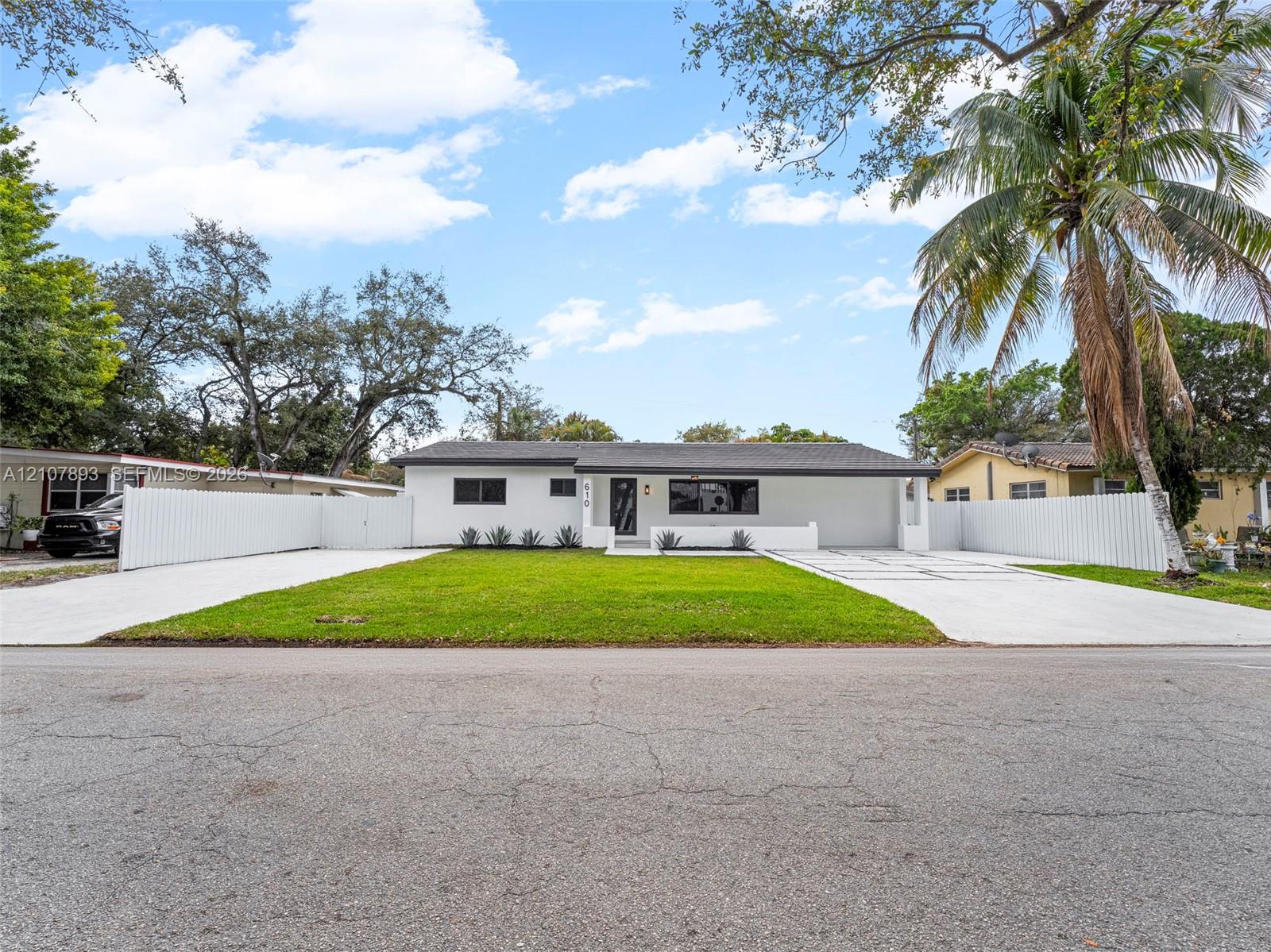 Single-story residence featuring a painted stucco exterior, dual concrete driveways, a central lawn, and surrounding white privacy fencing