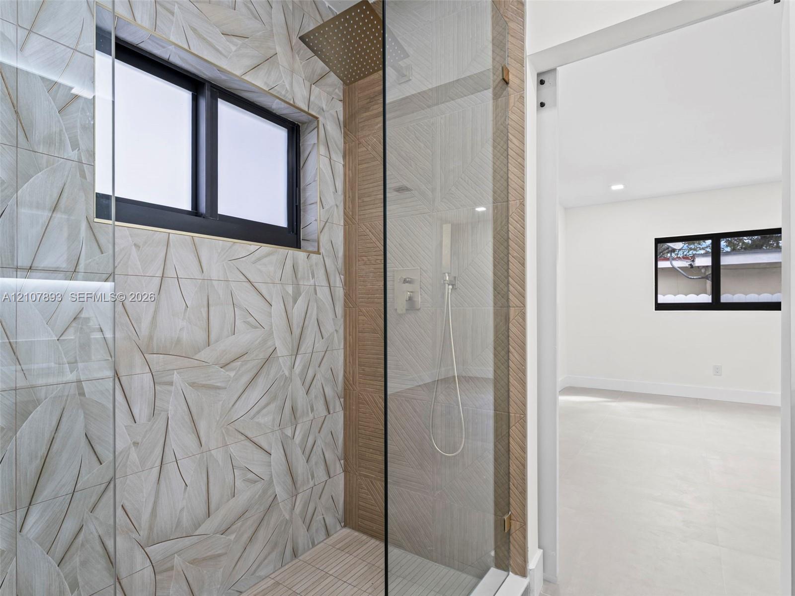 Walk-in shower featuring patterned tile walls, a rainfall showerhead, handheld fixture, and a frameless glass enclosure