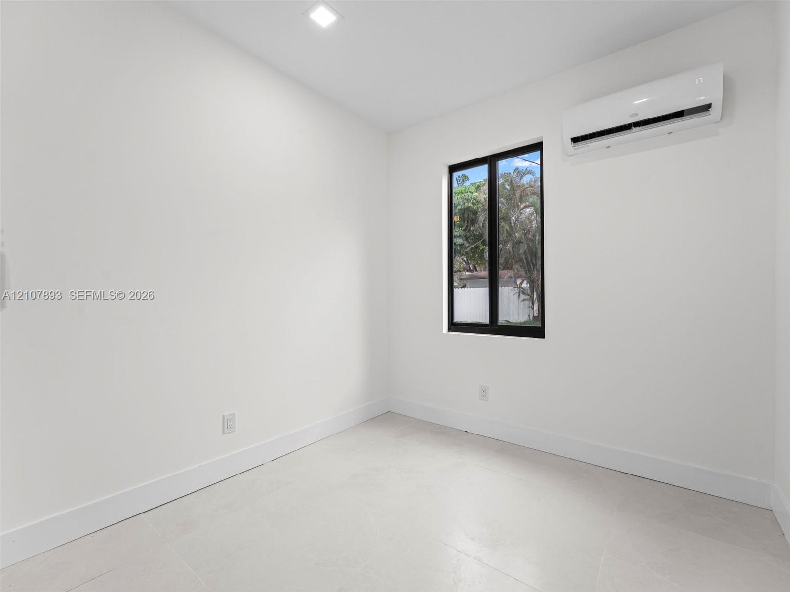 Interior space featuring white walls, light-colored tile flooring, a wall-mounted ductless air conditioning unit, recessed lighting, and a single window with a black frame