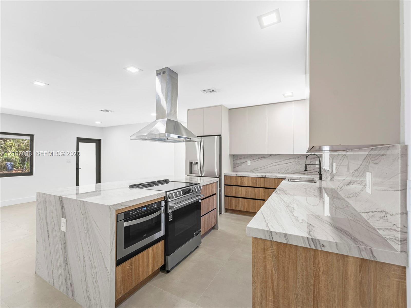 Kitchen featuring waterfall-edge stone countertops, wood-finish cabinetry, stainless steel range and built-in microwave, stainless steel chimney-style range hood, and tile flooring