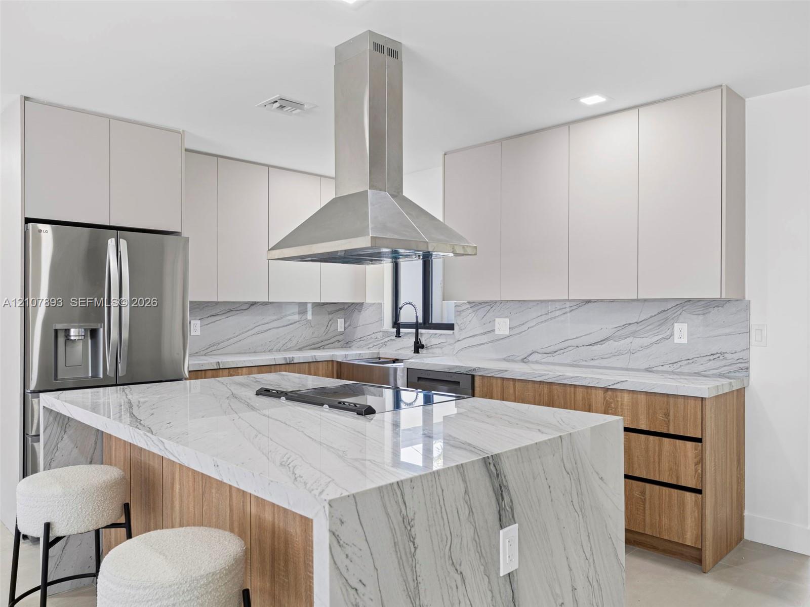 Kitchen featuring waterfall-edge stone countertops, stainless steel chimney-style range hood, dual-tone cabinetry, and wood-finish lower cabinetry