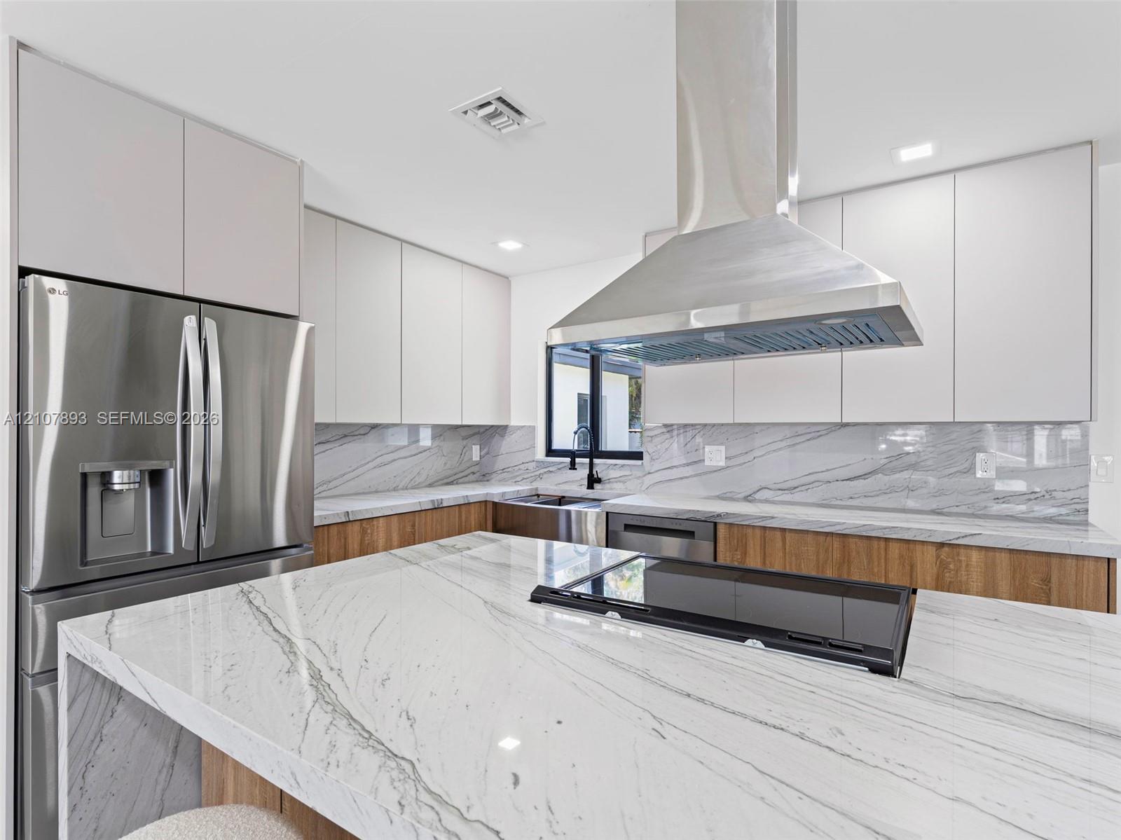 Kitchen featuring floor-to-ceiling flat-panel cabinetry, a central island with a stone countertop, a full-height stone backsplash, stainless steel appliances, and a stainless steel chimney-style range hood