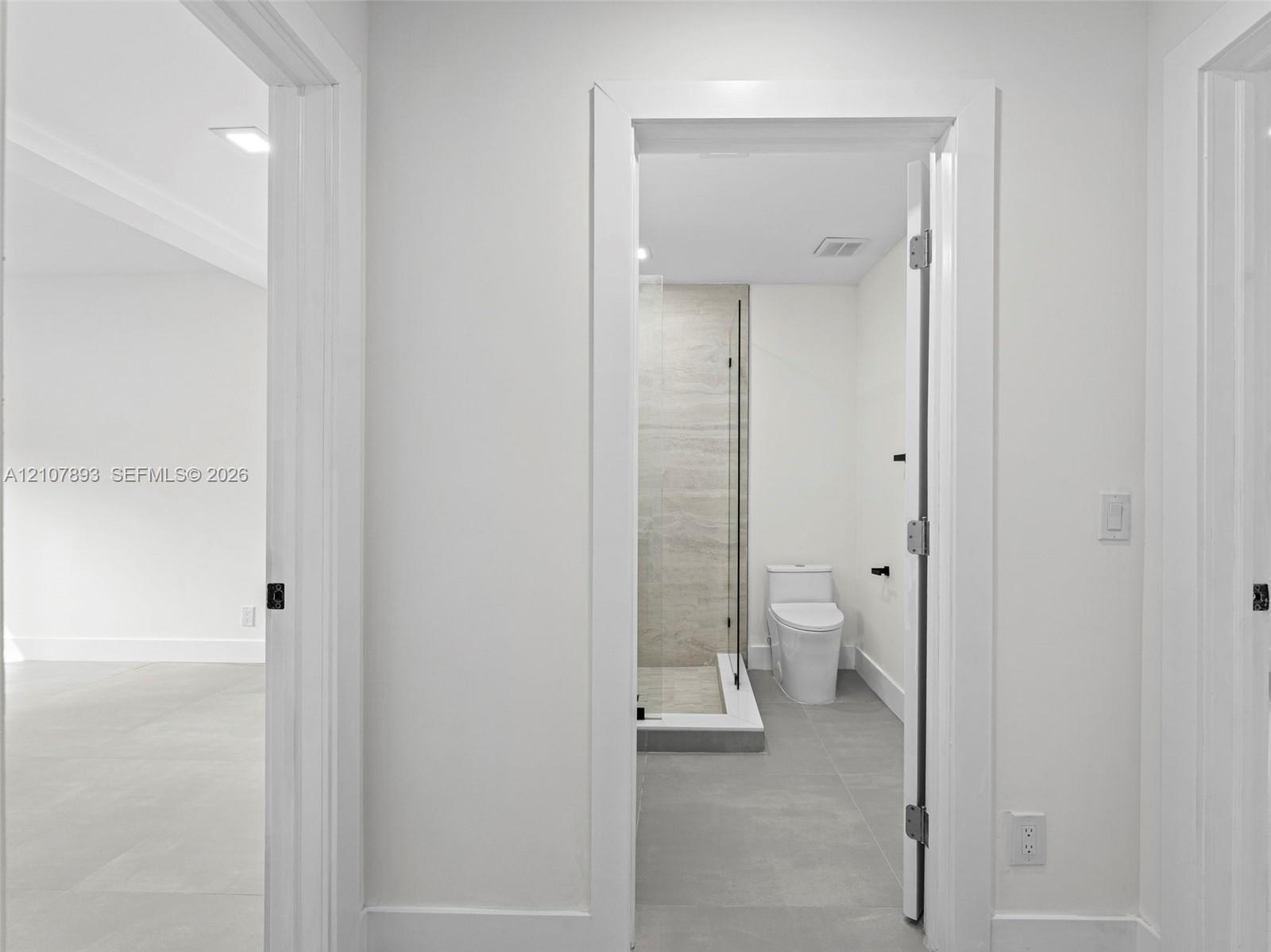 Bathroom featuring a glass-enclosed shower with large-format wall tile, a two-piece toilet, and grey tile flooring