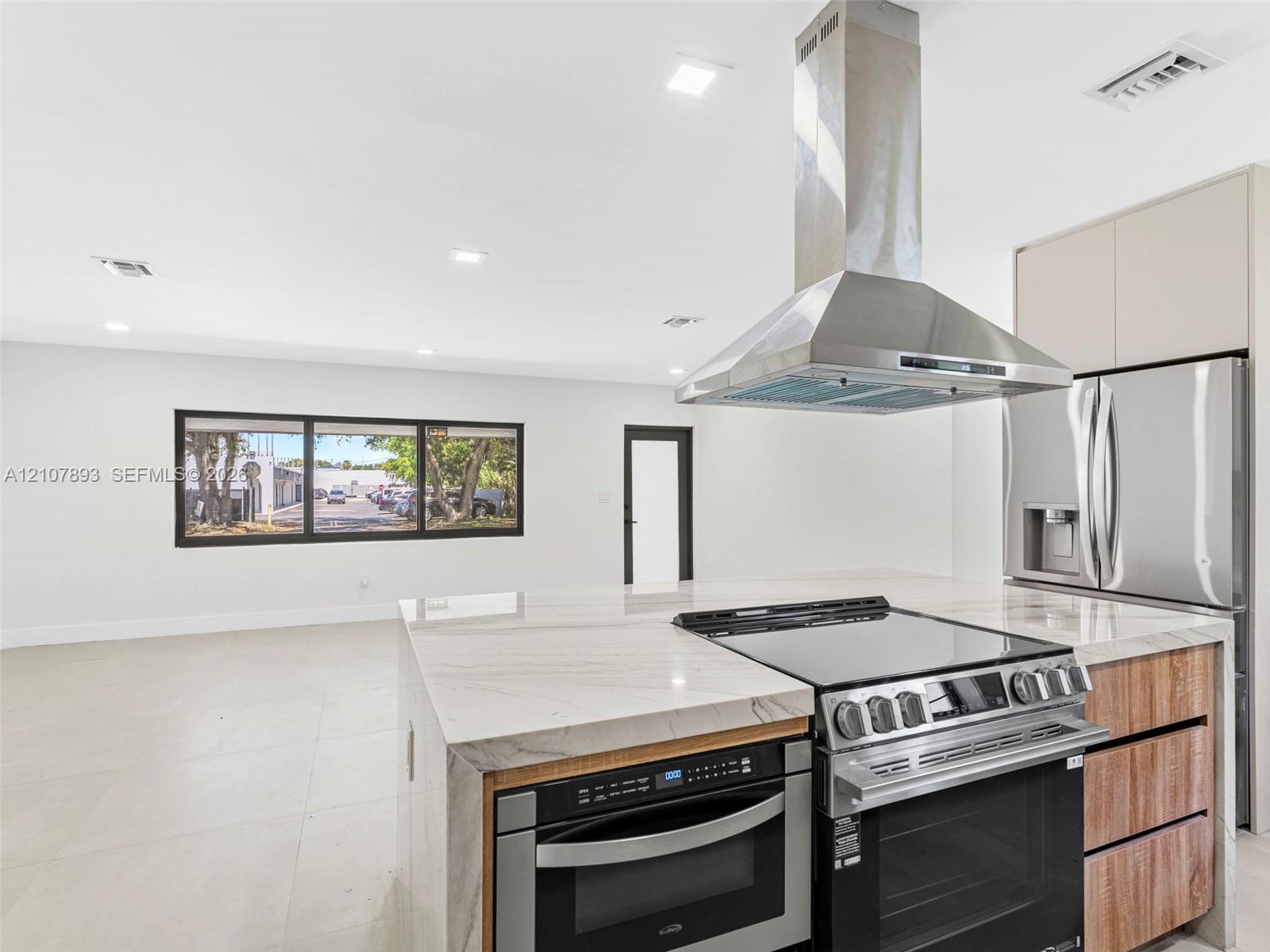 Kitchen featuring an island with a waterfall-edge countertop, stainless steel range hood, integrated built-in oven, and wood-finish cabinetry