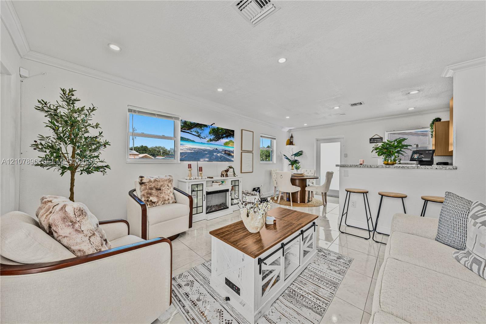 Open-concept living space featuring high-gloss tile flooring, recessed lighting, crown molding, and a breakfast bar with stone-finish countertops
