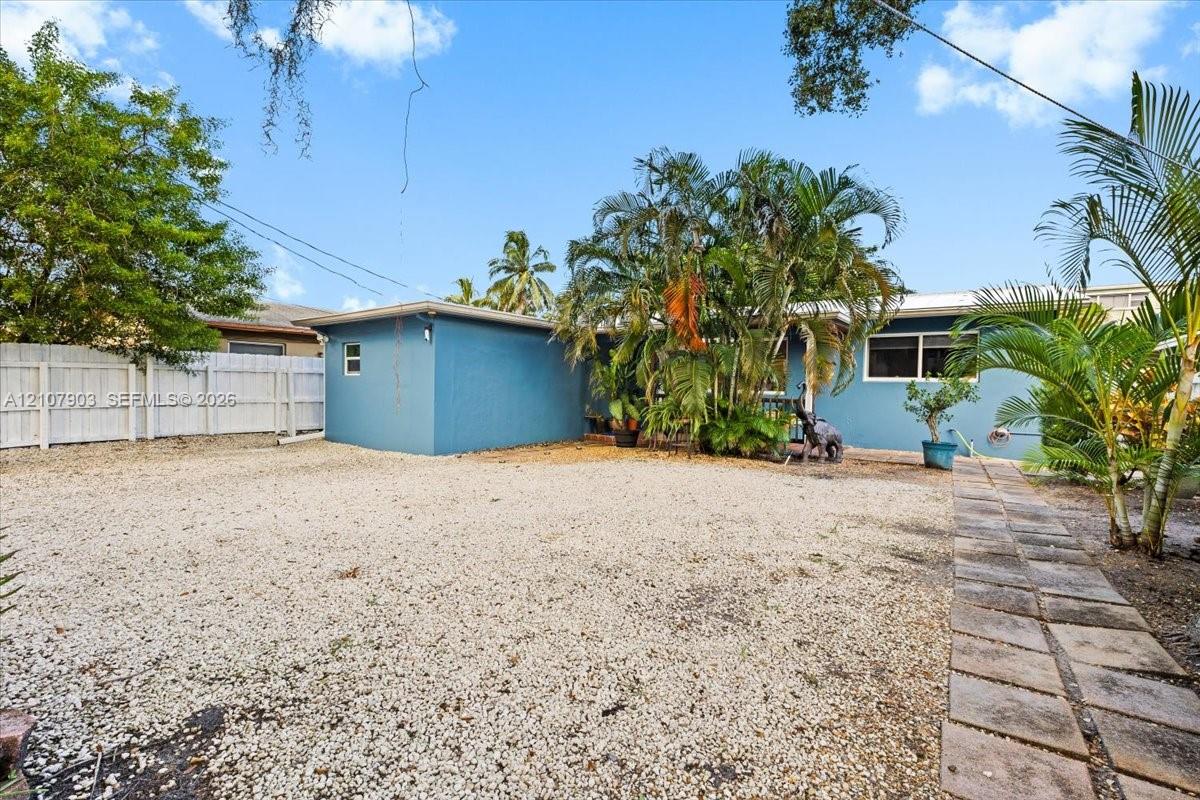 Spacious backyard featuring a gravel surface, concrete paver walkway, privacy fencing, and mature palm landscaping