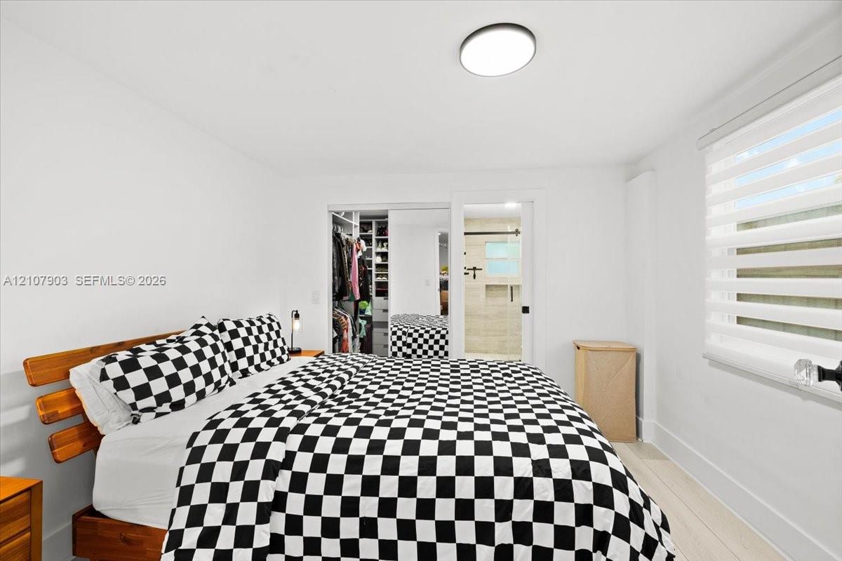 Bedroom featuring wood-finish flooring, dual sliding mirrored closet doors, built-in closet shelving, and roller-style window shades
