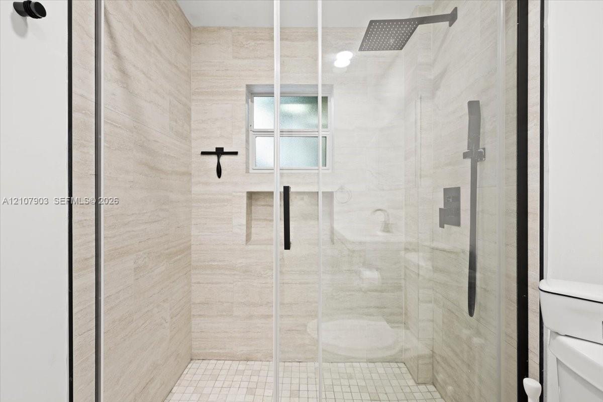Walk-in shower featuring floor-to-ceiling stone-finish tile, glass enclosure, recessed storage niche, overhead rainfall showerhead, and a mosaic tile floor