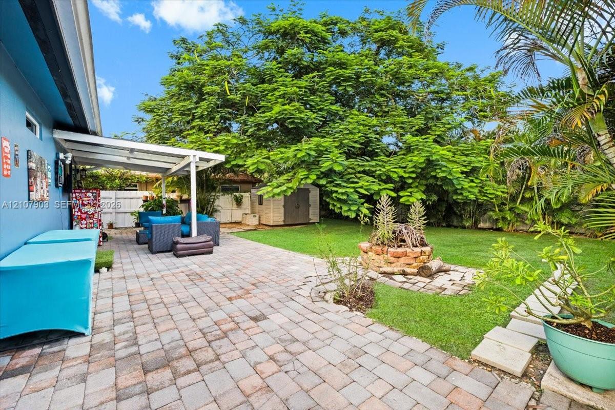 Backyard featuring a paved stone patio, covered pergola, natural stone fire pit, grass lawn, and mature trees