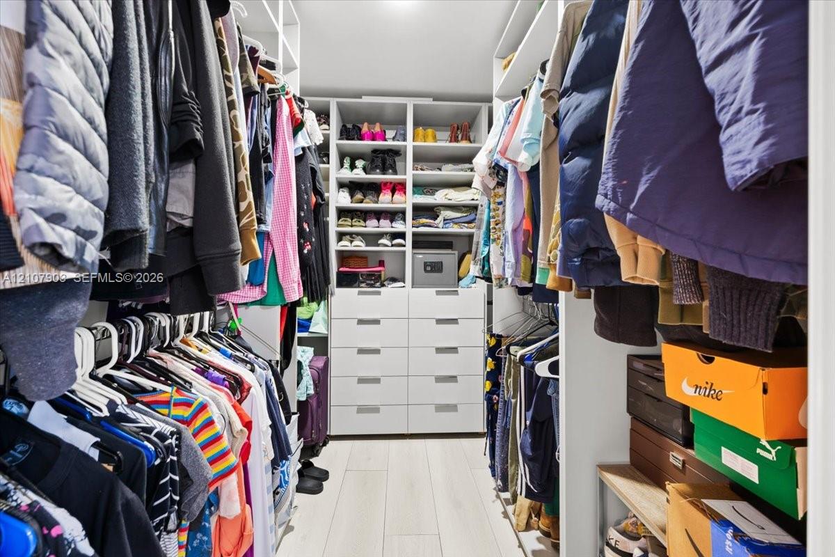 Custom walk-in closet featuring white built-in shelving, integrated dresser drawers with brushed metal pulls, and wood-finish flooring