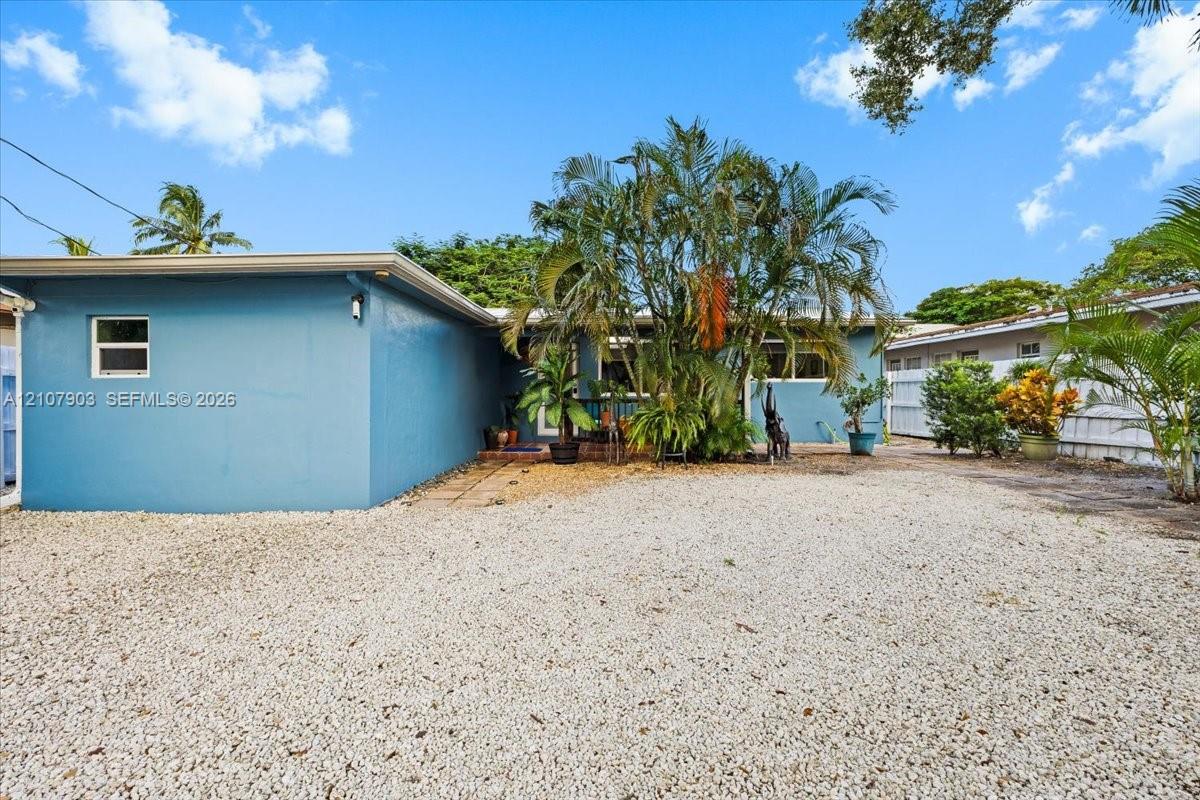 Exterior featuring light-blue painted stucco siding, stone-aggregate ground cover, and mature landscaping
