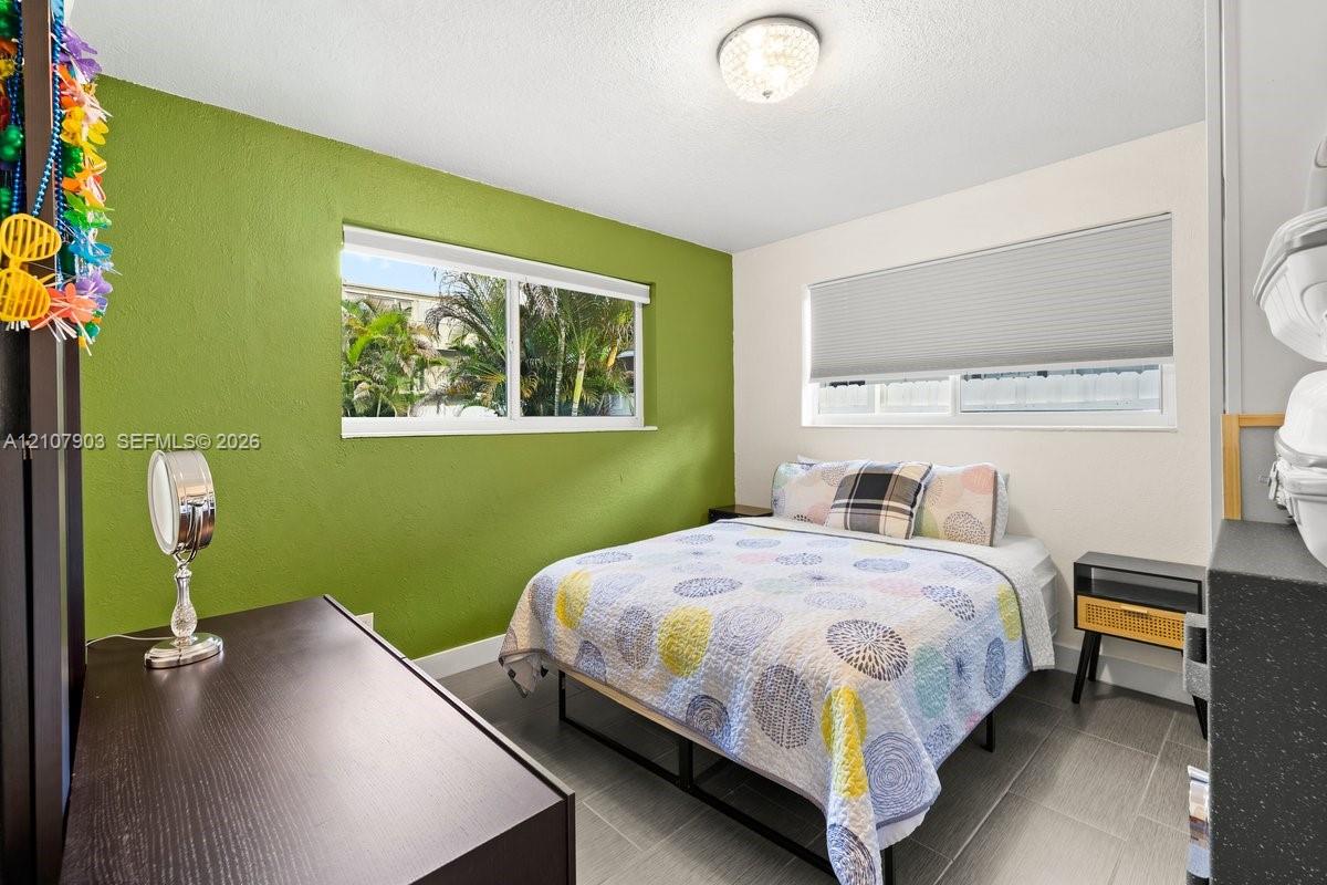 Room featuring large-format tile flooring, dual windows with fitted shades, and a flush-mount crystal-style light fixture