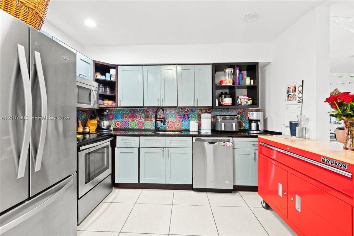 Kitchen featuring light blue cabinetry, patterned tile backsplash, stainless steel appliances, dark stone-finish countertops, and tile flooring