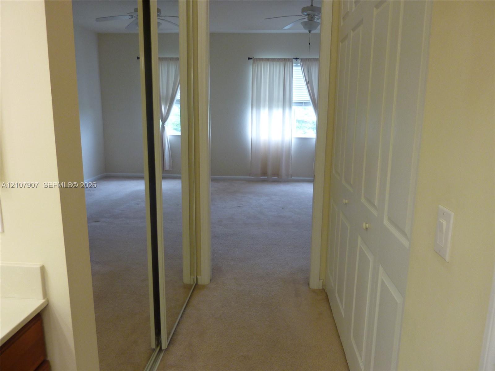 Hallway featuring dual sliding mirrored closet doors, a multi-panel interior door, and ceiling fan fixture
