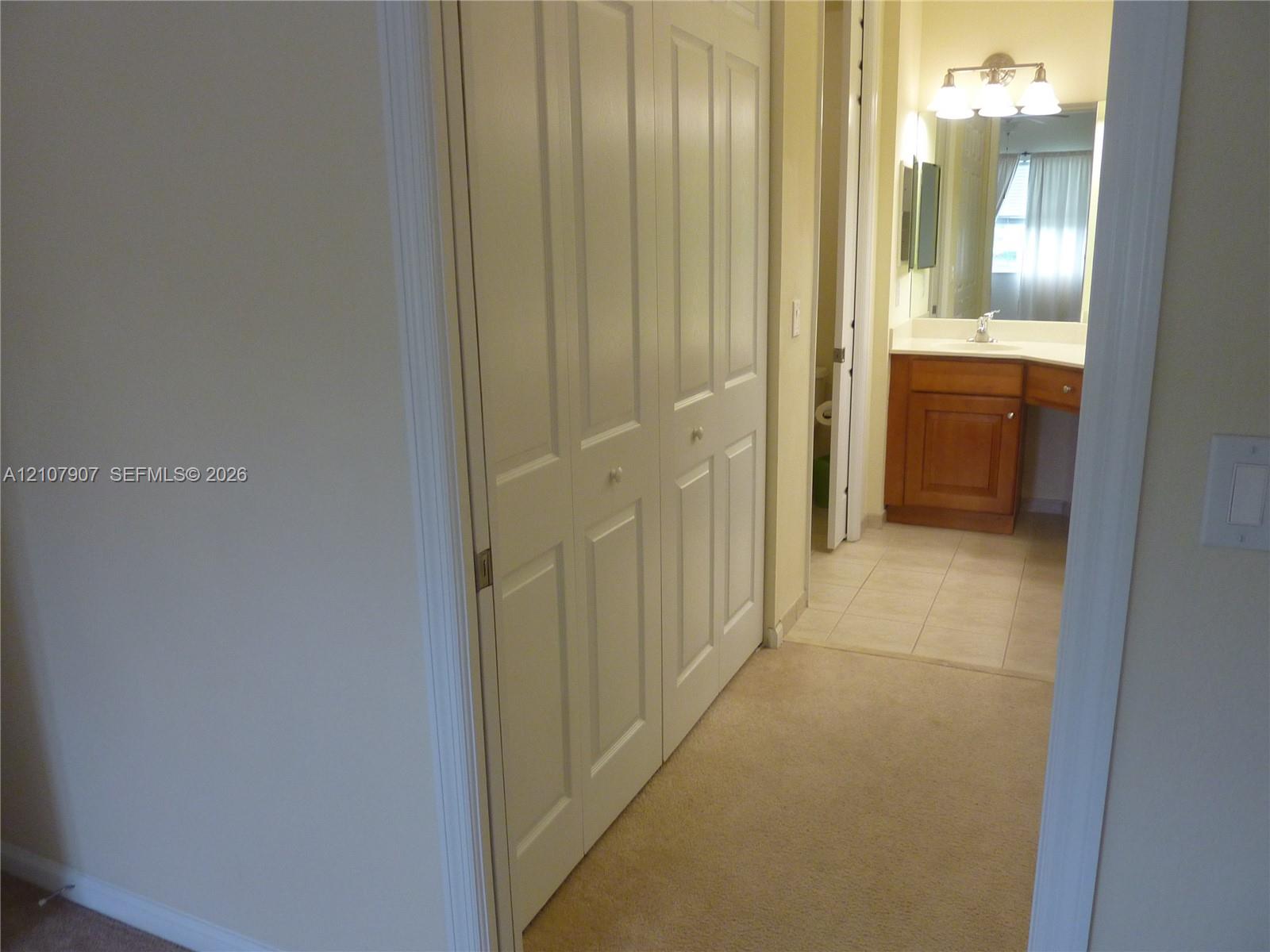 Double-door closet with white paneled finish, wood-finish vanity cabinet, ceramic tile flooring, and integrated vanity lighting