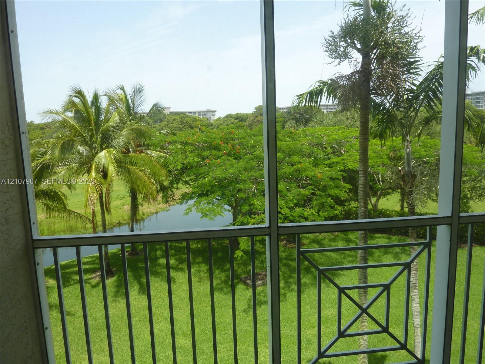 Screened-in balcony featuring metal railing, mature palm trees, water feature, and landscaped grounds