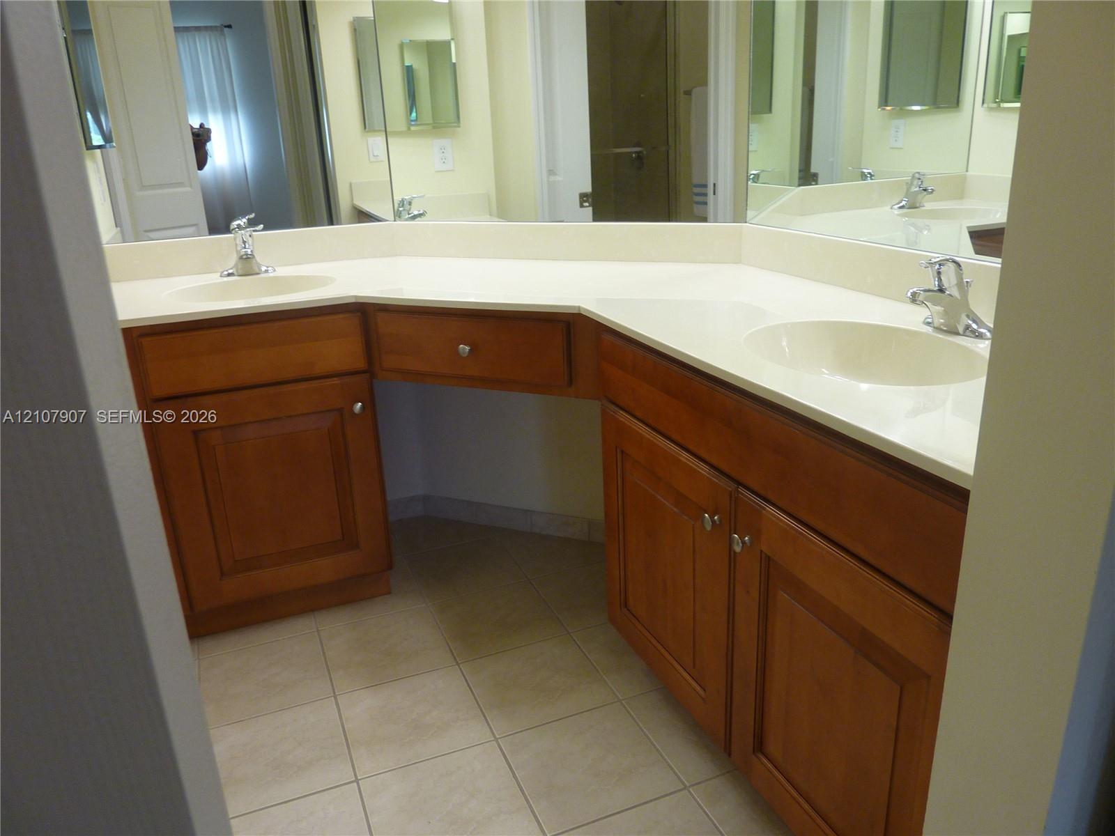 Dual-sink vanity with wood-finish cabinetry, solid-surface countertop, integrated basins, chrome fixtures, and a large-scale wall mirror