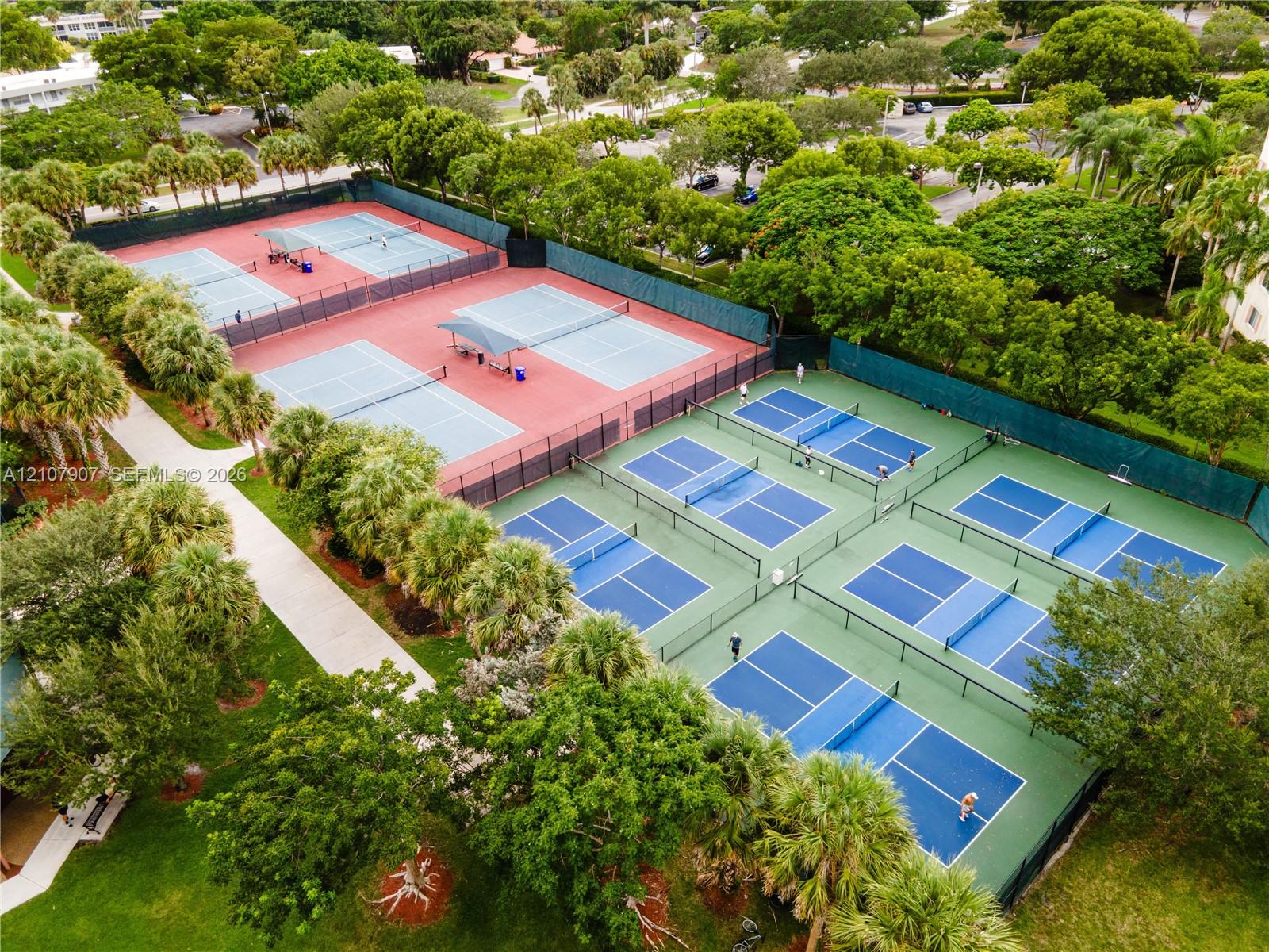 Outdoor recreation complex featuring multiple hard-surface tennis courts and integrated pickleball courts enclosed by perimeter fencing and surrounded by mature landscaping