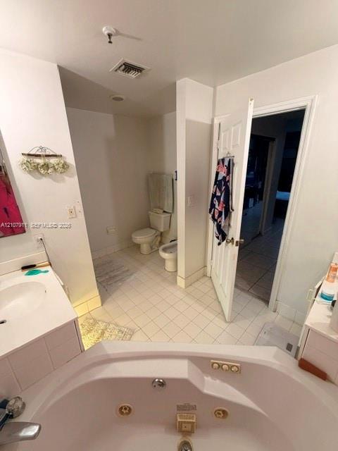 Bathroom featuring a white corner jetted soaking tub, tiled flooring, built-in vanity, toilet, and bidet